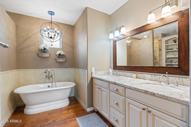 full bathroom featuring a soaking tub, wainscoting, wood finished floors, and a sink