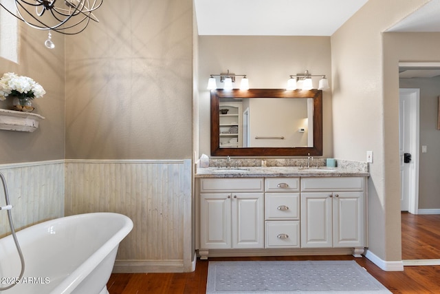 full bath featuring a wainscoted wall, a freestanding tub, wood finished floors, and a sink