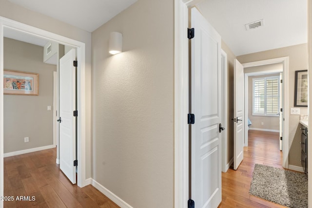 hall featuring visible vents, baseboards, and light wood-style floors