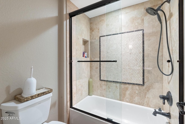 bathroom featuring toilet, a textured wall, and shower / bath combination with glass door