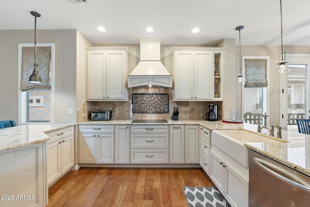 kitchen featuring a sink, a peninsula, light wood finished floors, custom exhaust hood, and dishwasher