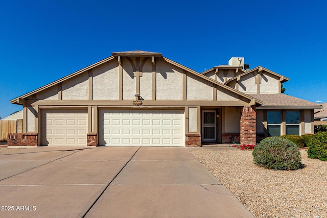 tudor home with concrete driveway, an attached garage, brick siding, and stucco siding