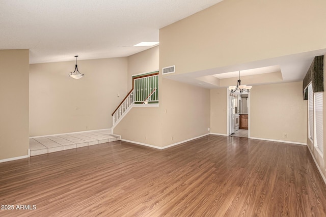 unfurnished living room with visible vents, baseboards, stairway, wood finished floors, and a raised ceiling