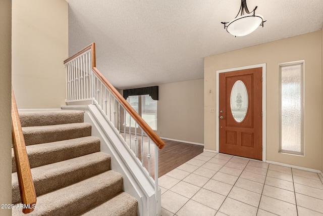 foyer with light tile patterned floors, stairway, baseboards, and a textured ceiling