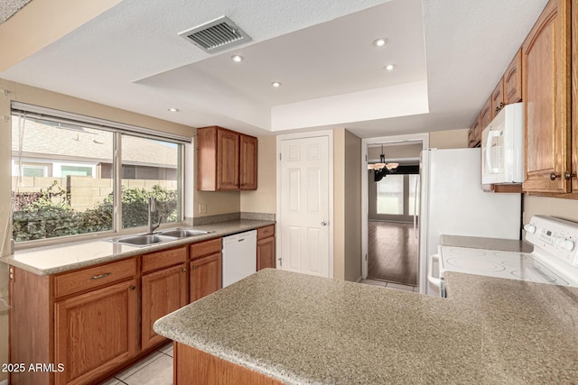 kitchen with white appliances, visible vents, a peninsula, a tray ceiling, and a sink