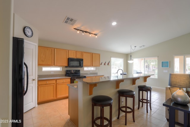 kitchen with decorative light fixtures, lofted ceiling, a kitchen breakfast bar, black appliances, and a center island with sink