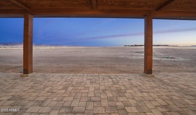 patio terrace at dusk with a water view and a view of the beach