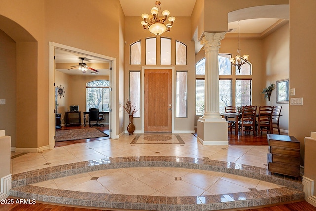 foyer entrance with ornate columns, a towering ceiling, ceiling fan with notable chandelier, and tile patterned floors