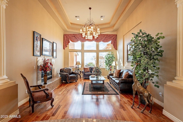 living room featuring a chandelier, a raised ceiling, hardwood / wood-style floors, and ornate columns