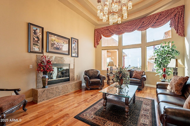 living room featuring wood-type flooring, a premium fireplace, a high ceiling, and a notable chandelier