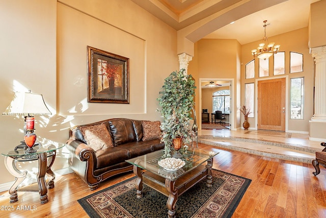 living room featuring decorative columns, a towering ceiling, a chandelier, and light hardwood / wood-style flooring