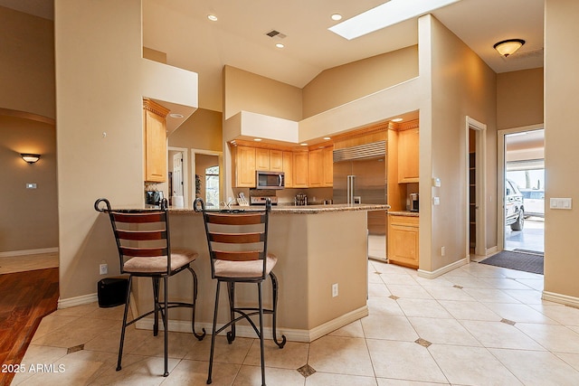 kitchen with appliances with stainless steel finishes, a breakfast bar, light tile patterned floors, kitchen peninsula, and light brown cabinets