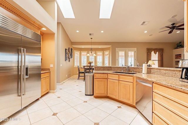 kitchen featuring pendant lighting, sink, appliances with stainless steel finishes, a skylight, and light brown cabinetry