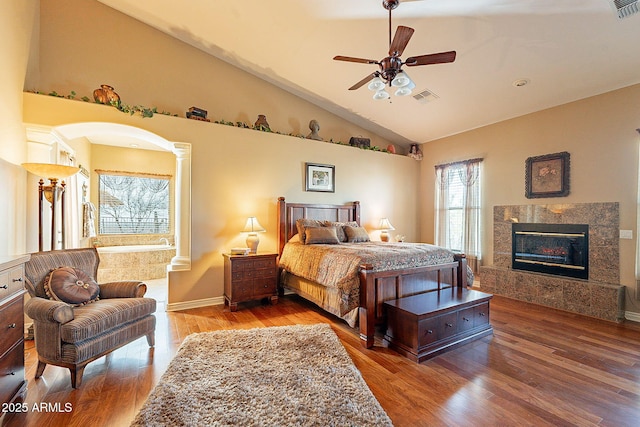 bedroom with hardwood / wood-style flooring, ceiling fan, a high end fireplace, and vaulted ceiling