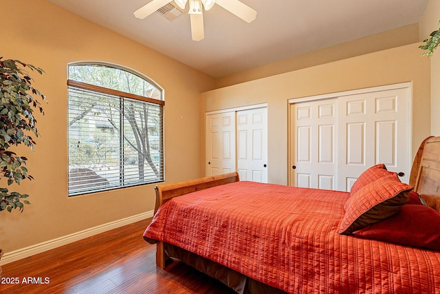 bedroom featuring multiple closets, vaulted ceiling, hardwood / wood-style floors, and ceiling fan