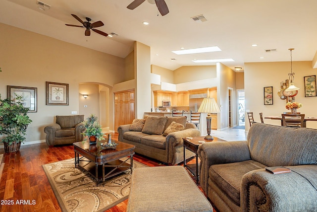 living room featuring ceiling fan, dark hardwood / wood-style floors, high vaulted ceiling, and a skylight