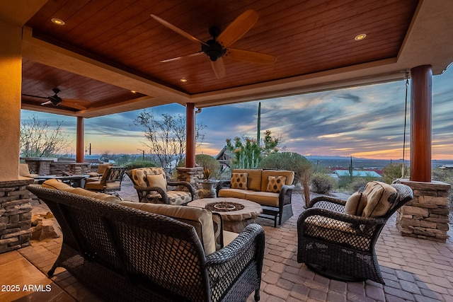 patio terrace at dusk featuring ceiling fan and an outdoor living space with a fire pit