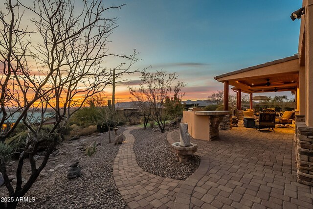 patio terrace at dusk featuring exterior bar, ceiling fan, and exterior kitchen