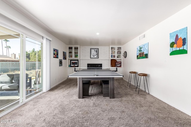 recreation room featuring a brick fireplace, built in shelves, and carpet flooring