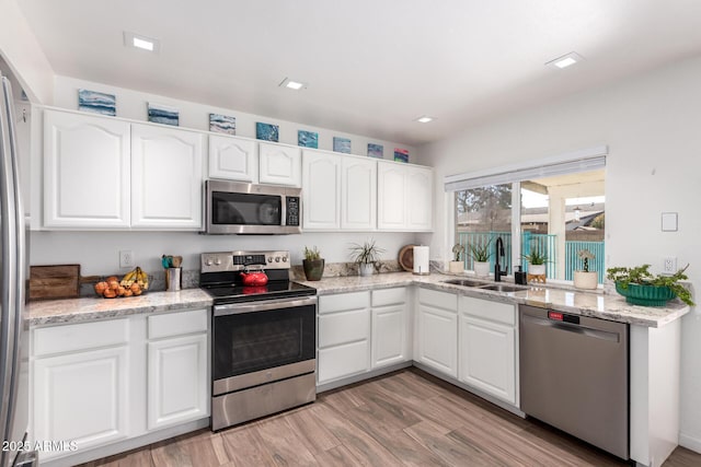 kitchen with sink, light hardwood / wood-style flooring, appliances with stainless steel finishes, white cabinetry, and light stone counters