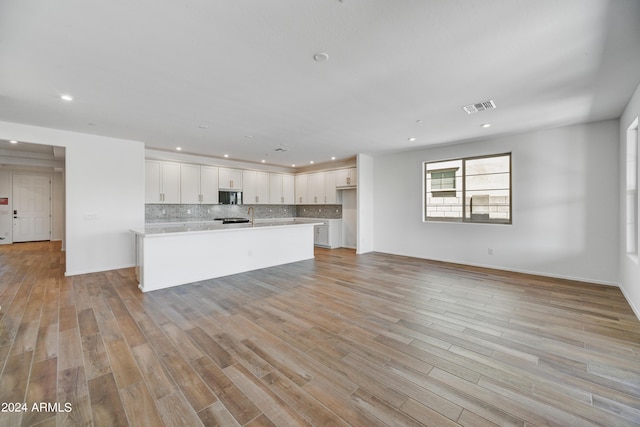 kitchen with backsplash, a kitchen island with sink, white cabinets, and light hardwood / wood-style floors