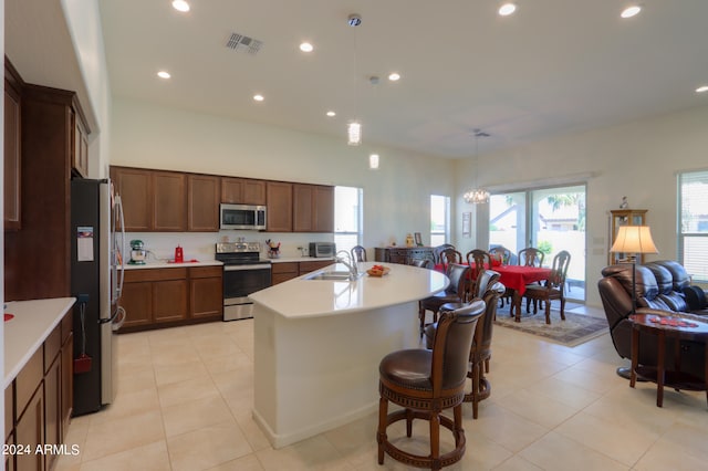 kitchen with hanging light fixtures, stainless steel appliances, a center island with sink, and light tile floors