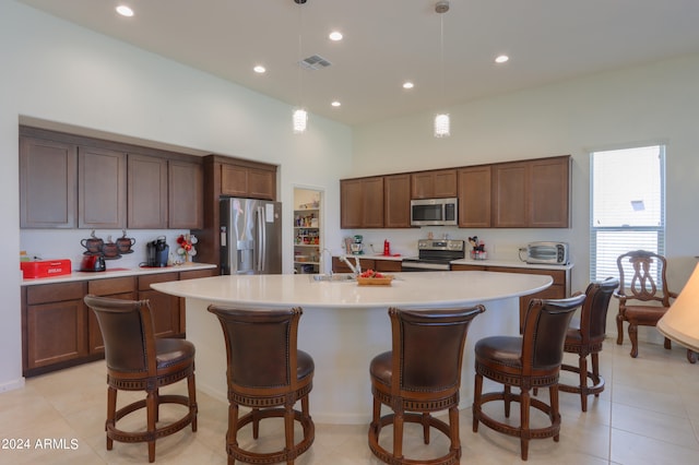 kitchen with light tile floors, hanging light fixtures, sink, a kitchen island with sink, and appliances with stainless steel finishes