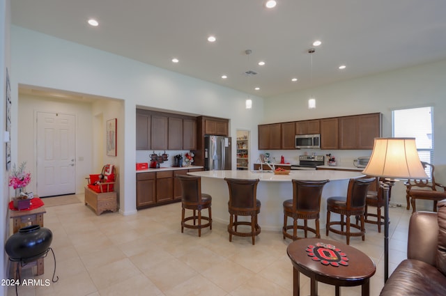 kitchen with a kitchen island with sink, appliances with stainless steel finishes, sink, light tile floors, and a breakfast bar