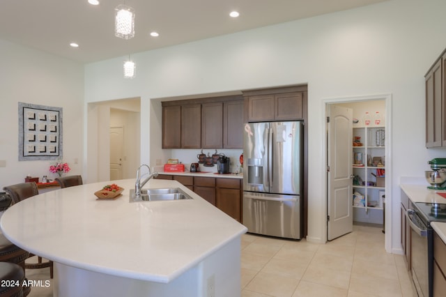 kitchen with a center island with sink, stainless steel refrigerator with ice dispenser, pendant lighting, sink, and light tile floors