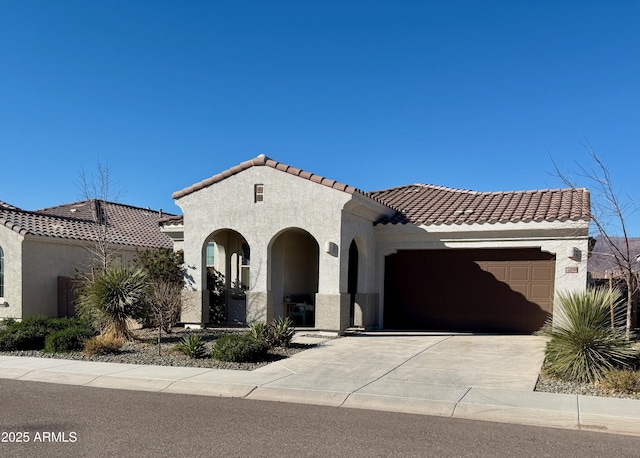 mediterranean / spanish house featuring concrete driveway, a tile roof, an attached garage, and stucco siding