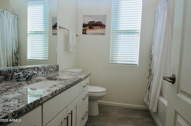 bathroom featuring toilet, vanity, a wealth of natural light, and baseboards