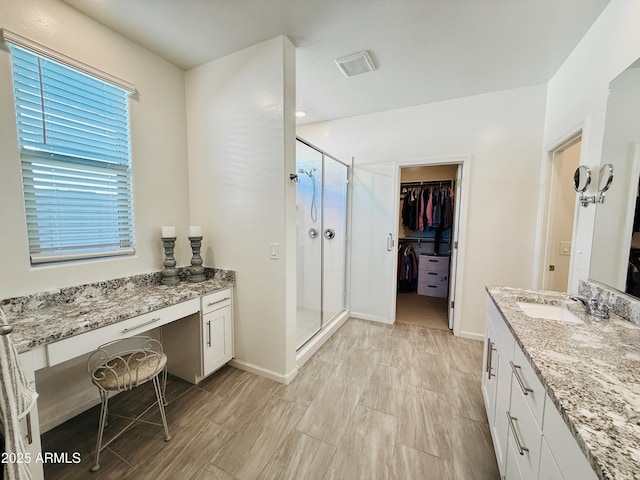 bathroom with a stall shower, a walk in closet, vanity, and baseboards