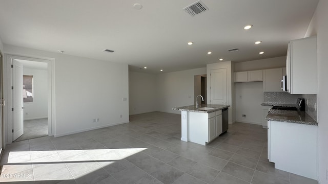 kitchen with sink, stainless steel appliances, white cabinets, a center island with sink, and dark stone counters