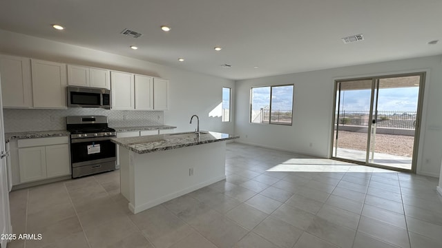 kitchen featuring sink, light stone counters, a center island with sink, appliances with stainless steel finishes, and backsplash