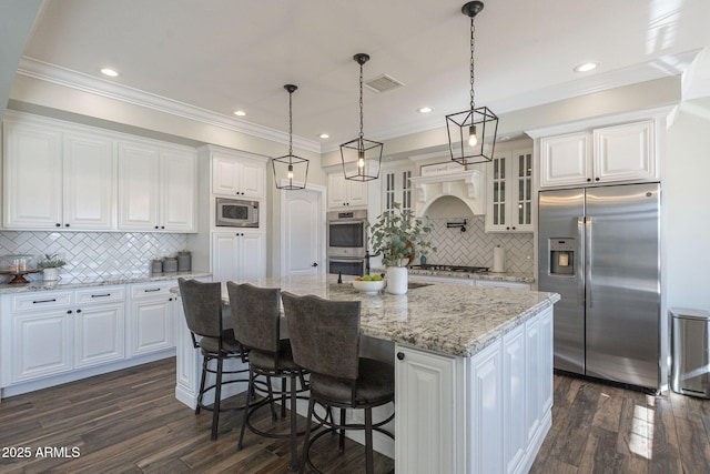 kitchen with an island with sink, appliances with stainless steel finishes, decorative backsplash, and white cabinetry