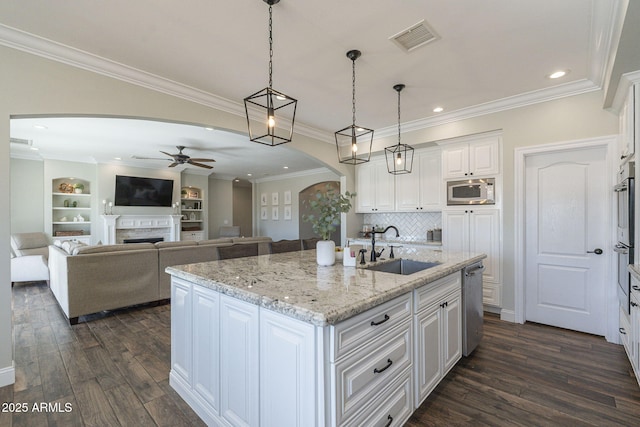 kitchen with an island with sink, light stone countertops, pendant lighting, white cabinets, and sink