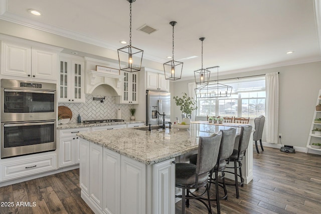 kitchen with stainless steel appliances, white cabinetry, a kitchen island with sink, and light stone counters