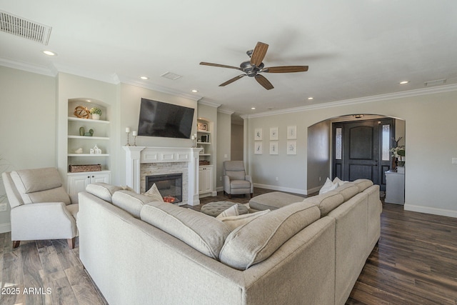 living room with crown molding, ceiling fan, dark wood-type flooring, a fireplace, and built in features