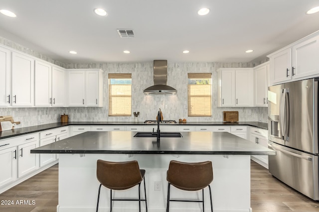 kitchen featuring an island with sink, stainless steel fridge, and wall chimney range hood