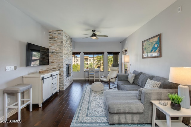 living room featuring dark wood-style flooring, ceiling fan, and a stone fireplace