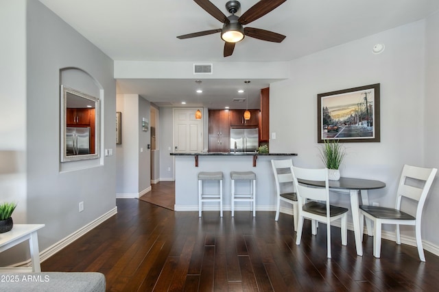 kitchen with built in refrigerator, dark wood-style floors, visible vents, and a breakfast bar area