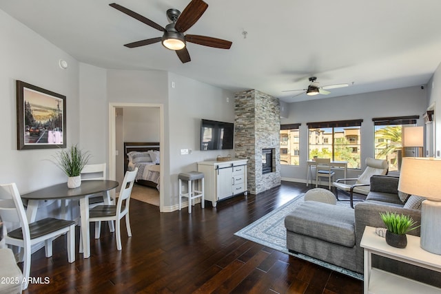 living room with baseboards, a ceiling fan, wood finished floors, and a stone fireplace