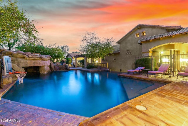 pool at dusk featuring pool water feature and a patio