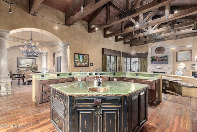 kitchen featuring beam ceiling, ornate columns, high vaulted ceiling, decorative light fixtures, and a center island with sink