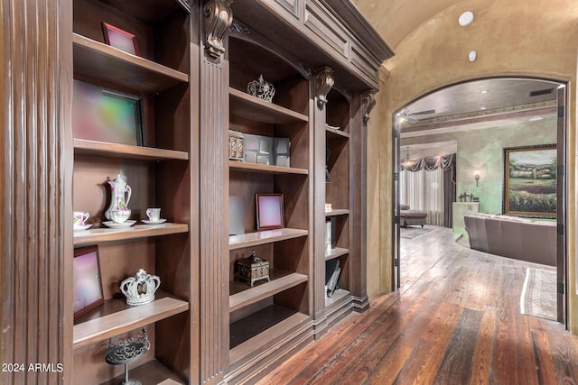 hallway with vaulted ceiling, built in shelves, and dark hardwood / wood-style floors