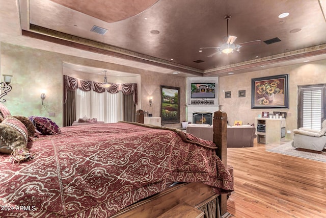 bedroom featuring a tray ceiling, multiple windows, ceiling fan, and light hardwood / wood-style flooring