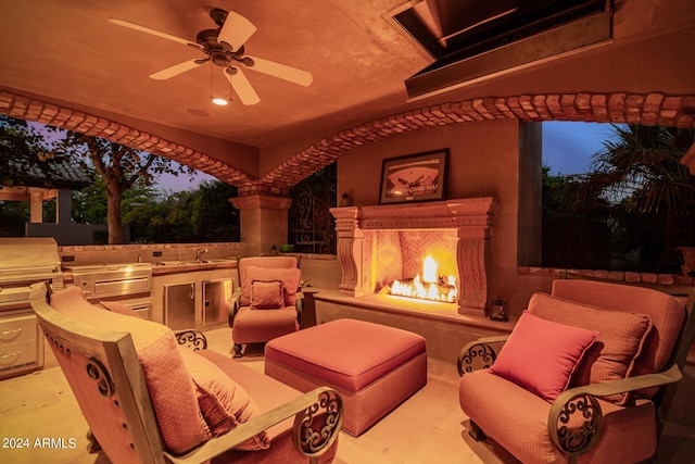 patio terrace at dusk with an outdoor kitchen, ceiling fan, an outdoor fireplace, and sink