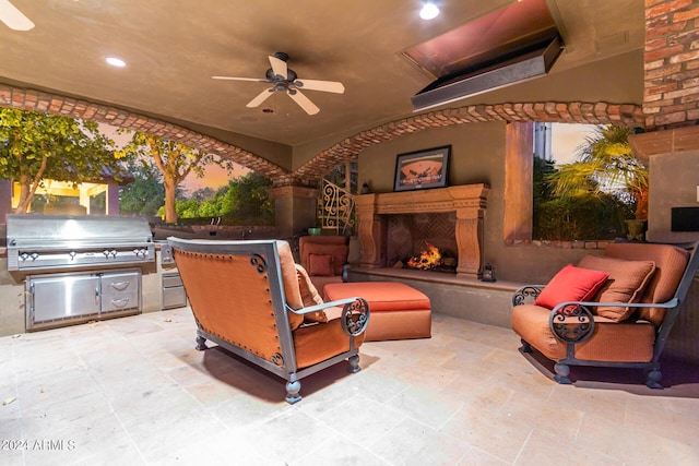 patio terrace at dusk featuring ceiling fan, area for grilling, and exterior fireplace