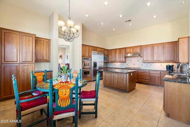 kitchen featuring sink, built in appliances, decorative light fixtures, decorative backsplash, and a kitchen island