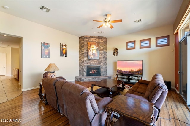 living room featuring a stone fireplace, ceiling fan, and wood-type flooring